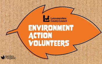 The Environment Action volunteer scheme logo. Whie Text reading "Environment Action Volunteers" overlayed onto an orange leaf.