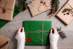 Image of a wrapped Christmas present held between a pair of hands, with part view of four other presents surrounding. 